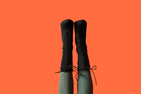 Legs of young woman in stylish black shoes on orange background