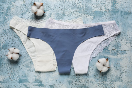 Set of female panties and cotton flowers on color background