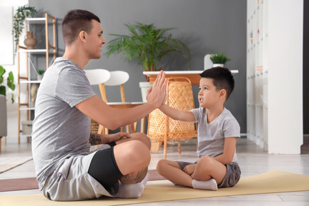 Sporty young man with his little son giving each other high-five at homeの写真素材