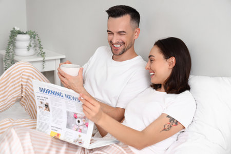 Young couple reading morning newspaper in bedroomの写真素材