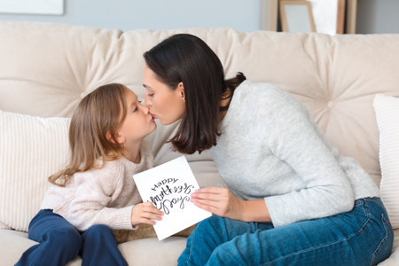 Cute little daughter greeting her beautiful mother with gift card at home. Happy Mother's Dayの写真素材