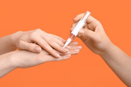 Female hands applying cuticle oil with pen on orange background, closeupの写真素材