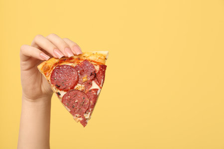 Female hand holding tasty pizza slice on yellow backgroundの写真素材