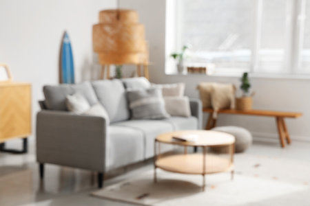 Stylish interior of light living room with comfortable sofa, table, carpet and lamp, blurred viewの写真素材