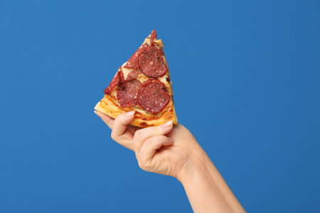 Female hand holding tasty pizza slice on blue backgroundの写真素材