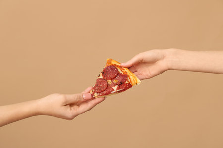 Female hand giving tasty pizza slice on beige backgroundの写真素材