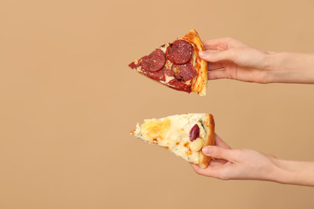 Female hands holding tasty pizza slices on beige backgroundの写真素材