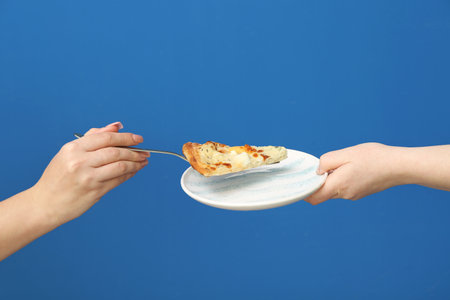 Female hand putting tasty pizza slice into plate on blue backgroundの写真素材