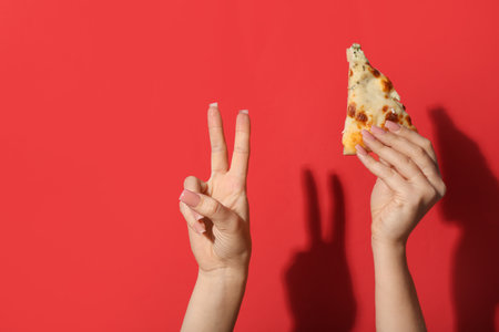 Female hand holding tasty pizza slice and making piece symbol on red backgroundの写真素材