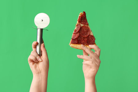 Female hands holding tasty pizza slice and pizza cutter on green backgroundの写真素材