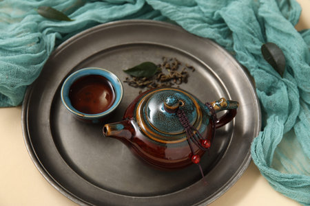 Tray with teapot and cup of tea on beige background