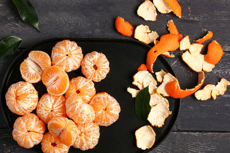 Plate with peeled tangerines and leaves on black wooden backgroundの写真素材