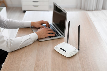 Businessman with wi fi router using laptop at table in office, closeup