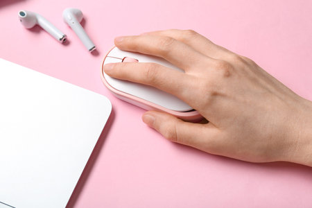 Female hand with modern computer mouse and earphones on pink background, closeup