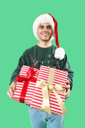 Happy young man in Santa hat with gift boxes on green backgroundの写真素材