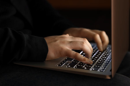 Hacker using laptop in dark room, closeup