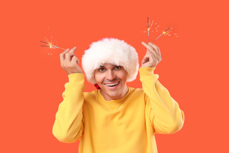 Happy young man in Santa hat with sparklers on orange backgroundの写真素材