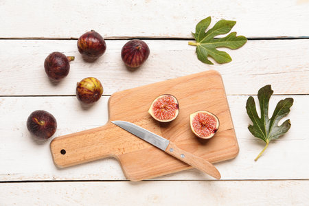 Board with halves of fresh ripe figs and leaves on white wooden backgroundの写真素材