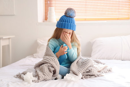 Sick little girl with hot water bottle sneezing in bedroomの写真素材