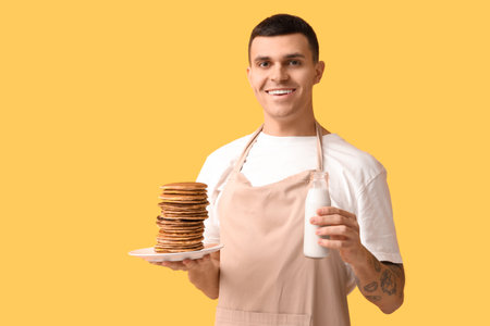 Young man with tasty homemade pancakes and milk on yellow backgroundの写真素材