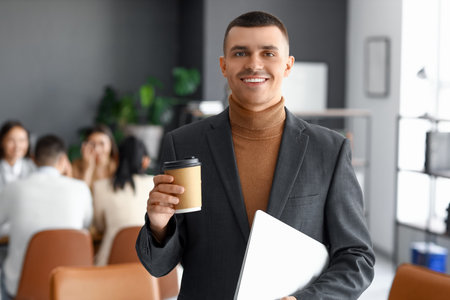 Businessman with cup of coffee and laptop in conference hallの写真素材