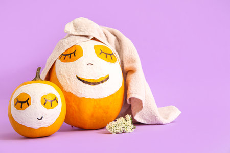 Pumpkins with drawn faces, masks and flowers on lilac backgroundの写真素材