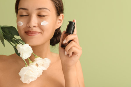 Beautiful Asian woman with facial cream and flowers on green background, closeupの写真素材