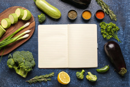 Composition with blank recipe book, fresh vegetables and spices on dark color backgroundの写真素材
