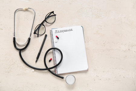 Notebook with the word MENOPAUSE, pills, stethoscope and eyeglasses on light backgroundの写真素材