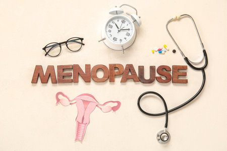 Word MENOPAUSE with stethoscope, paper uterus, eyeglasses and alarm clock on light backgroundの写真素材