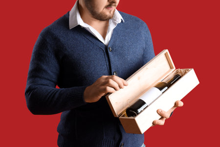 Sommelier holding box with bottle of wine on red backgroundの写真素材