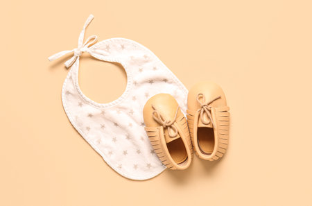 Stylish baby shoes with bib on beige backgroundの写真素材