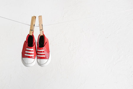 Stylish baby shoes hanging on rope against grunge white backgroundの写真素材