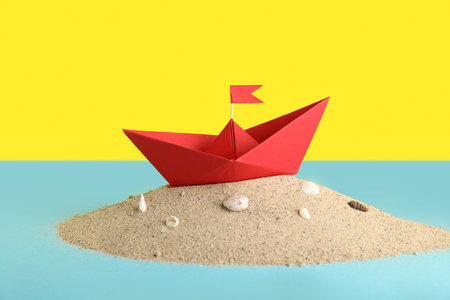 Red origami boat with sand and seashells on color backgroundの写真素材
