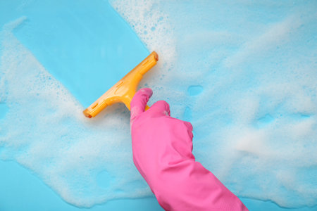 Female hand in rubber glove cleaning blue surface with squeegee