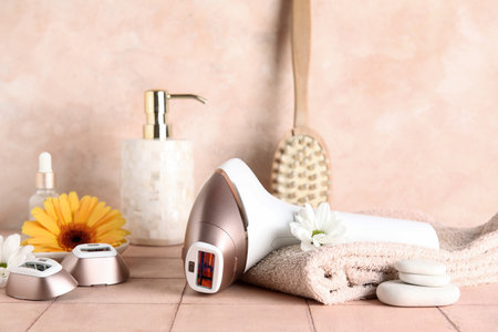 Modern photoepilator with bath supplies, cosmetic products, attachments and flowers on pink tile table near wallの写真素材