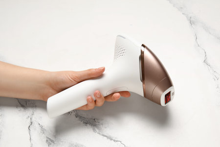 Female hand with modern photoepilator on grunge white background