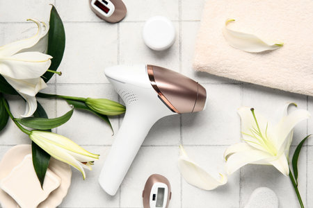 Modern photoepilator with attachments, bath supplies and lily flowers on white tile backgroundの写真素材