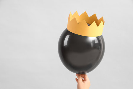 Woman holding black balloon with paper crown on light background. Birthday celebration, closeupの写真素材