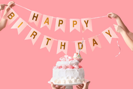 Female hands with tasty birthday cake and garland on pink backgroundの写真素材