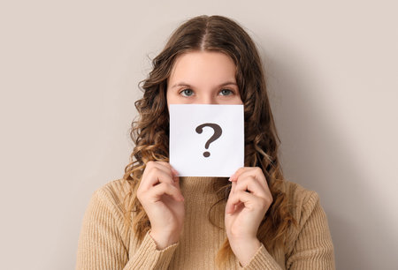 Young woman holding paper sheet with question mark on gray backgroundの写真素材