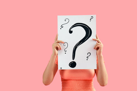 Young woman holding paper sheet with question marks on pink backgroundの写真素材