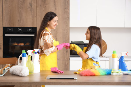 Happy mother with her little daughter bumping fists while cleaning in kitchenの写真素材