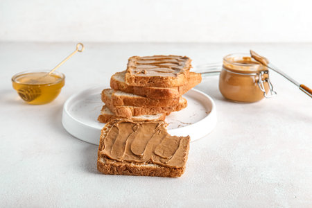 Plate of toasts with peanut butter and bowl of honey on white background