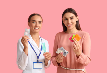 Female gynecologist and patient with contraceptives on pink backgroundの写真素材