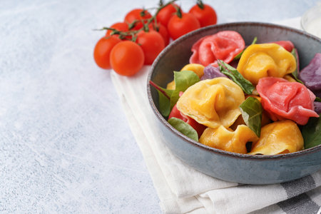 Bowl of boiled colorful dumplings with spinach and tomatoes on white backgroundの写真素材