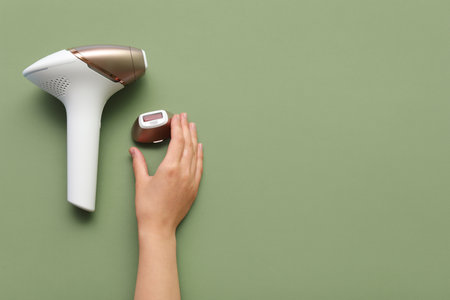 Female hands with modern photoepilator attachment on green backgroundの写真素材