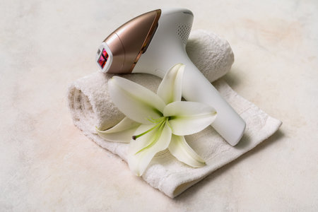 Modern photoepilator with lily flower and bath towel on grunge white backgroundの写真素材