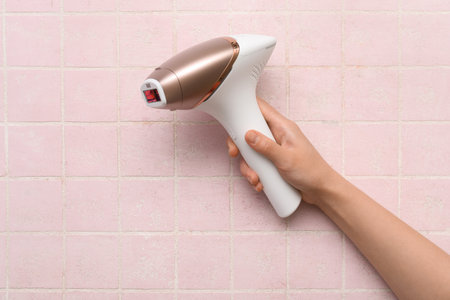 Female hand with modern photoepilator on pink tile backgroundの写真素材