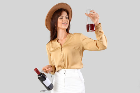Beautiful young woman with bottle and glass of wine on light backgroundの写真素材
